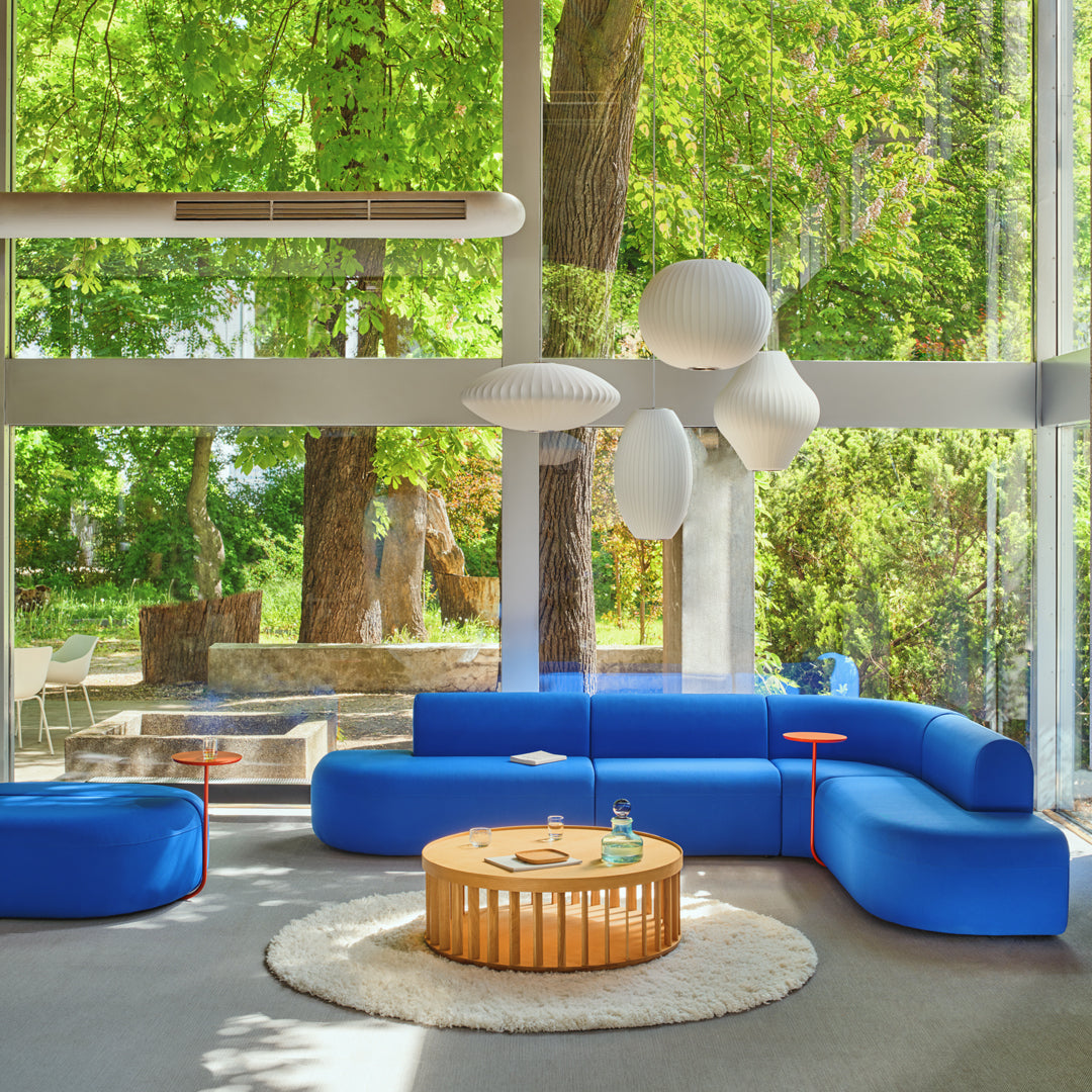 "Vibrant blue sectional sofa with white accents, round wooden coffee table, and plush circular rug in a modern setting."