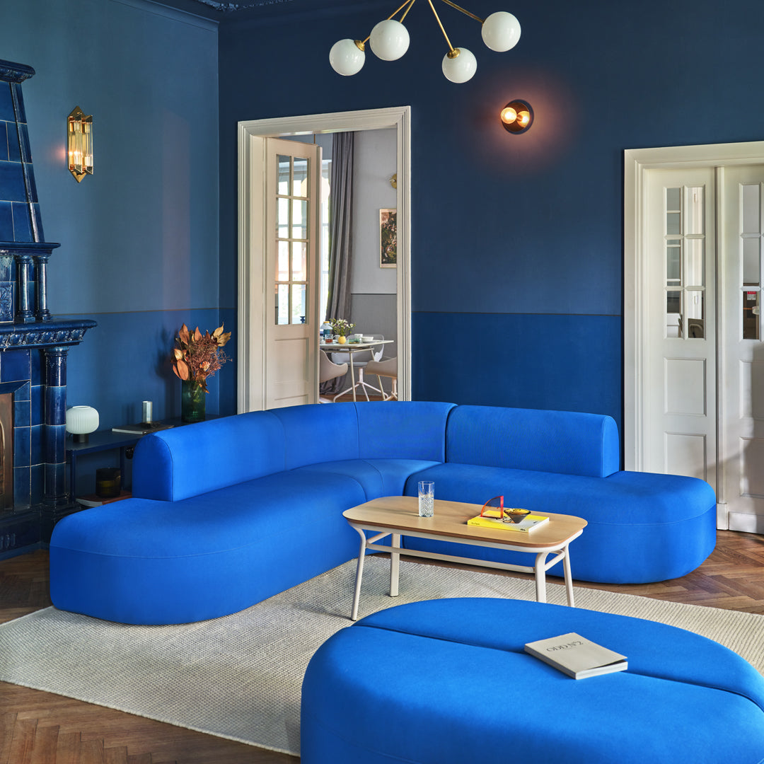 Vibrant blue curved sofa set against dark blue walls, complemented by light wood accents and a neutral rug.