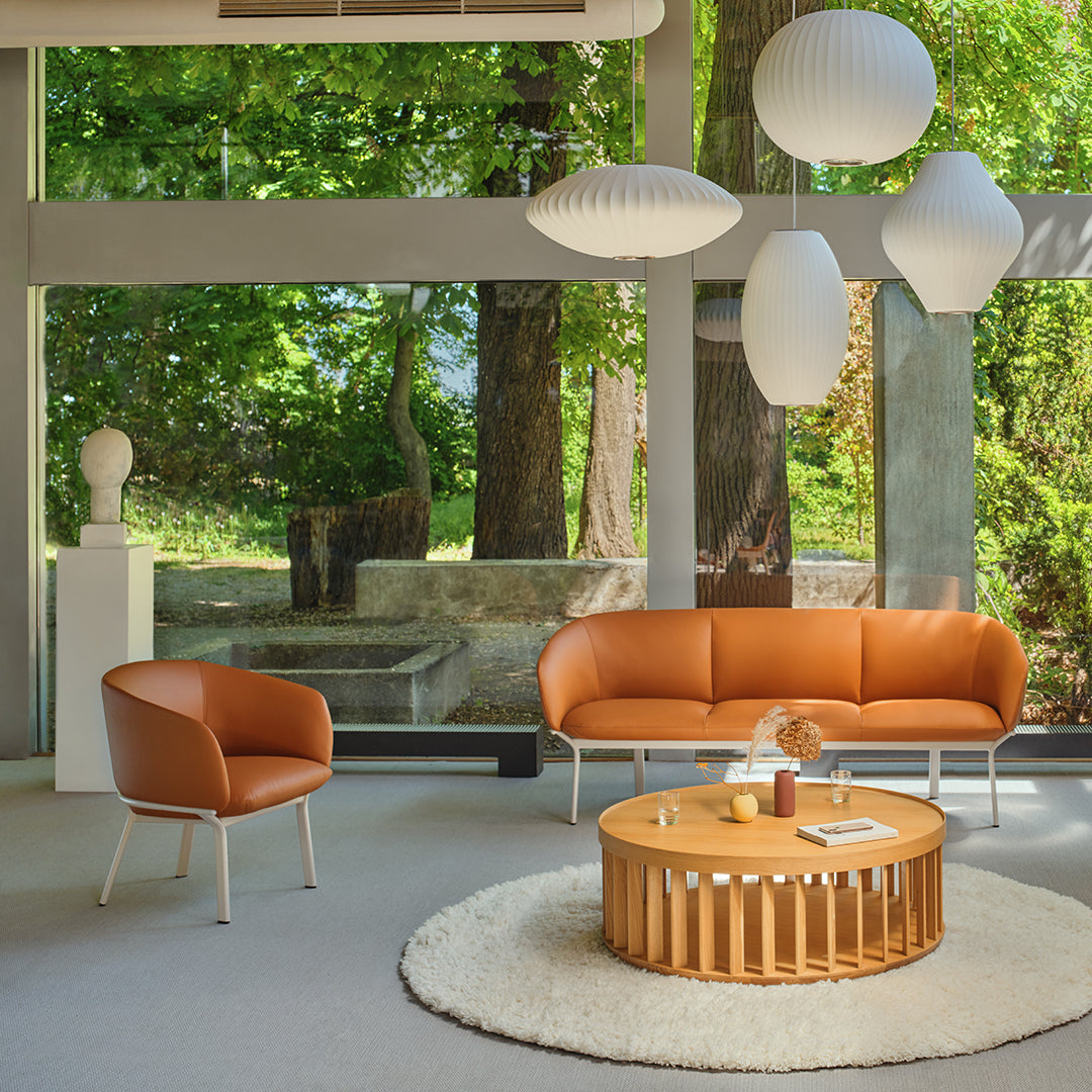 Stylish orange leather sofa and chair, round wooden coffee table, and soft white rug in a bright, modern setting.