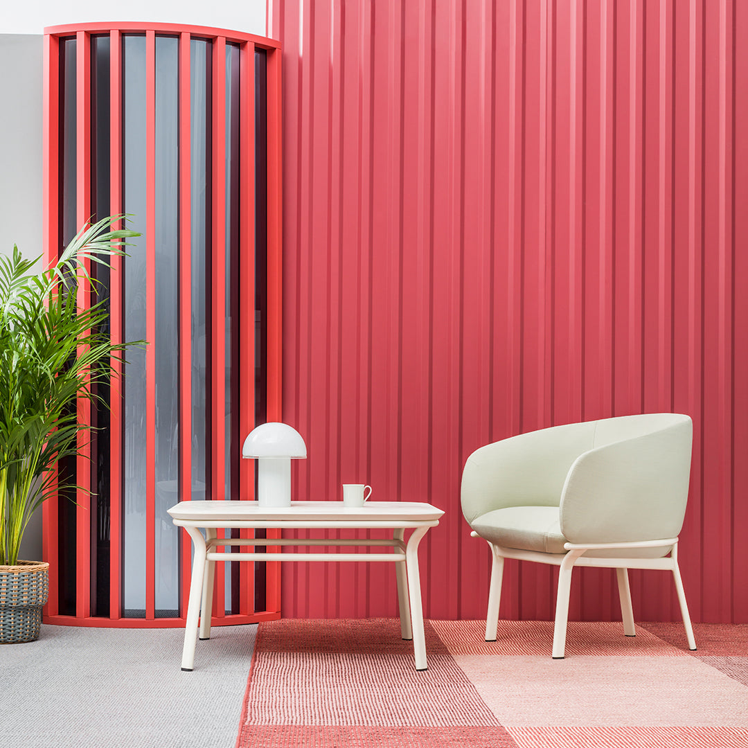 Modern living space featuring a coral-colored wall, white chair, and geometric pink carpet pattern. Elegant, vibrant decor.