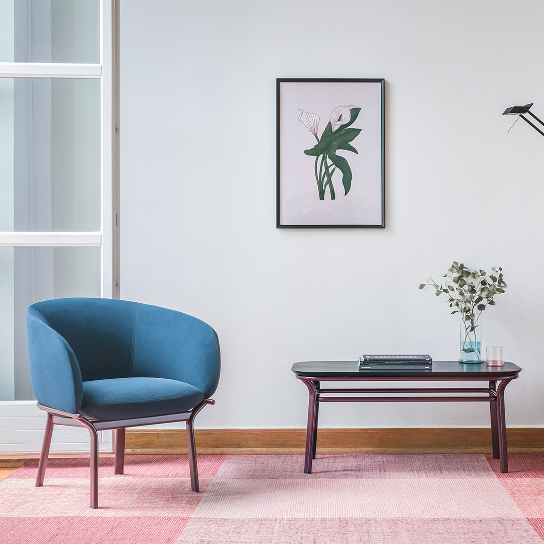 Modern blue chair on a soft pink and beige patterned rug, complemented by a sleek black coffee table.