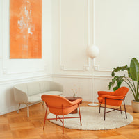 Modern living room decor with orange chairs, neutral sofa, and white walls, featuring geometric patterns and warm tones.