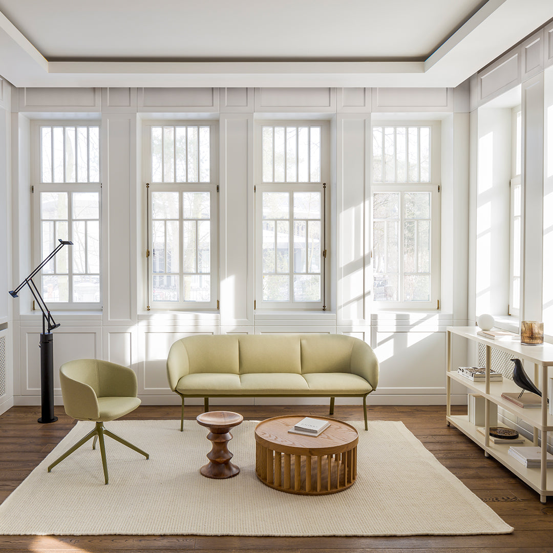 "Light green sofa and chair on a beige rug in a bright, modern room with white walls and large windows."