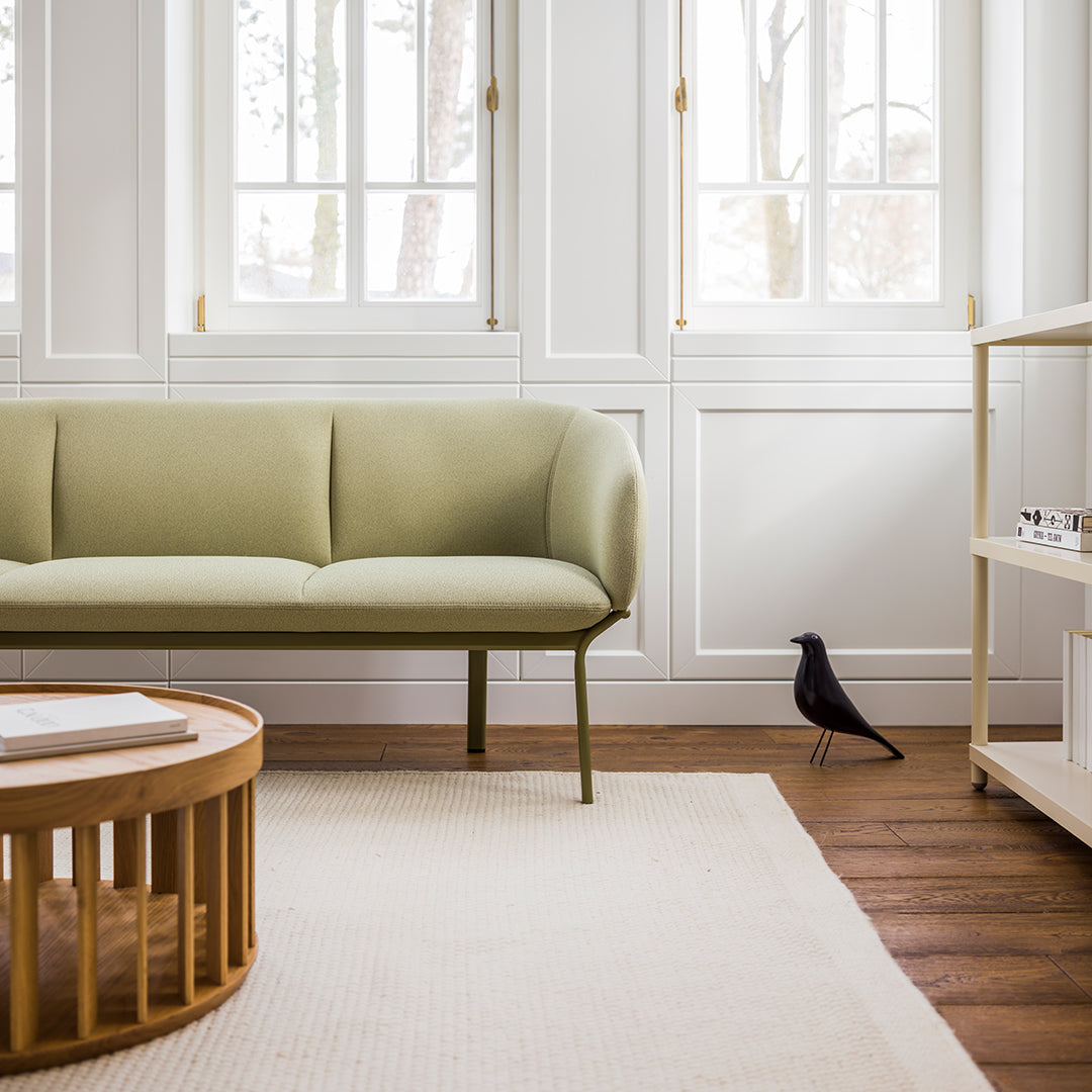 Muted olive green sofa with a sleek design, paired with natural wood accents and a textured beige rug.