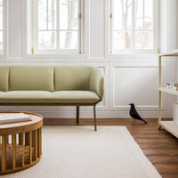 Muted olive green sofa with a sleek design, paired with natural wood accents and a textured beige rug.
