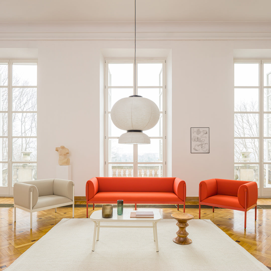 Bright orange and soft beige sofas with a minimalistic white pendant light in a light-filled, modern room.