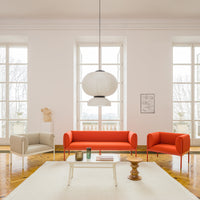 Bright orange and soft beige sofas with a minimalistic white pendant light in a light-filled, modern room.