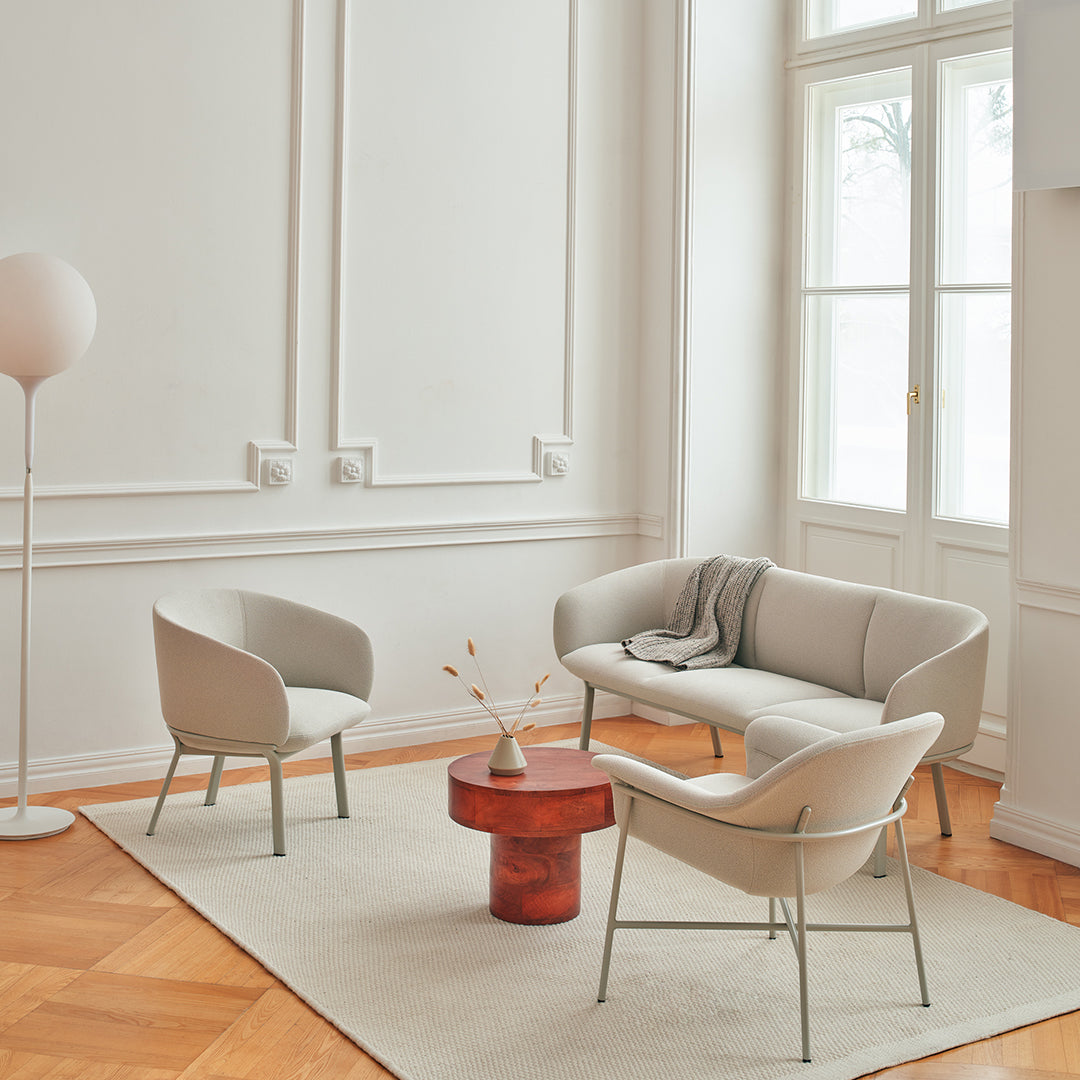 Light gray furniture with soft curves, a warm red table, and neutral beige rug in an elegant, bright room.
