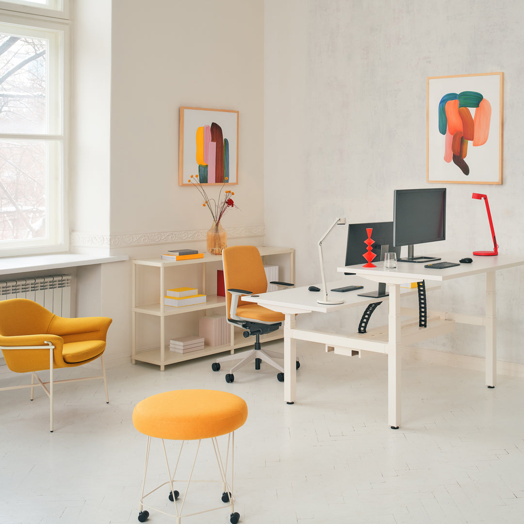 Modern office scene featuring yellow accent chairs and stools, with abstract art in orange and muted tones on white walls.