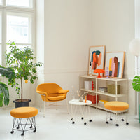Modern living space featuring vibrant orange chairs, abstract art in bold colors, and green plants in a light setting.