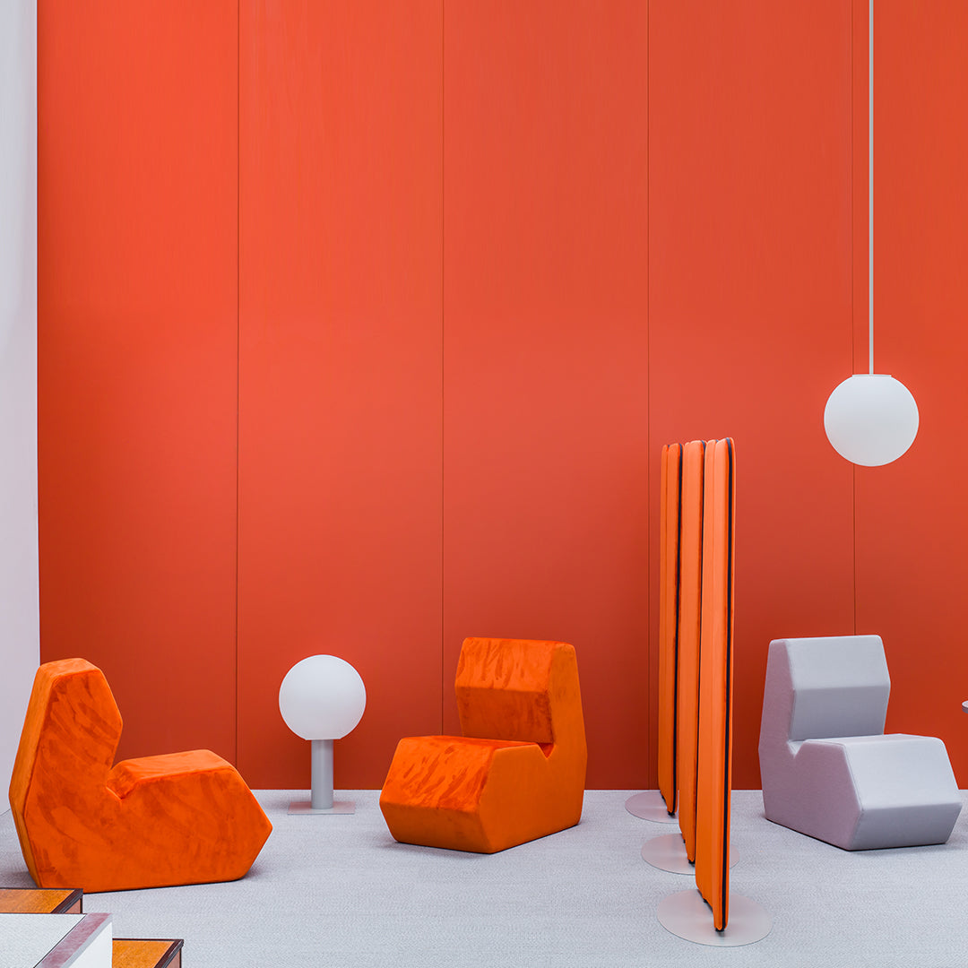 Vibrant orange and gray geometric furniture against a bold orange wall, with a round white lamp. Modern design aesthetic.