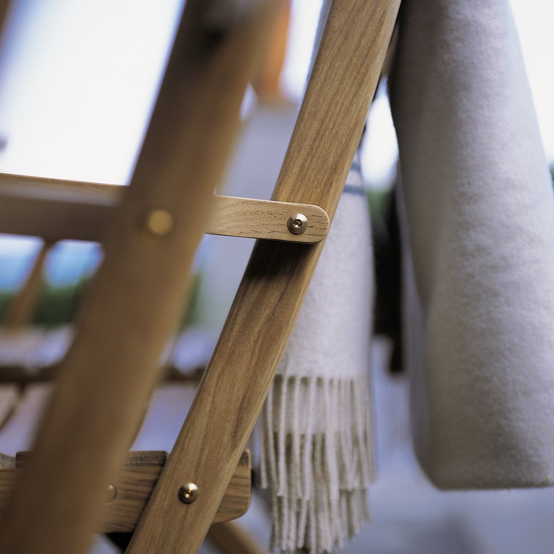 Cozy cream blanket draped on a natural wood chair, featuring delicate fringed edges. Perfect for outdoor relaxation.
