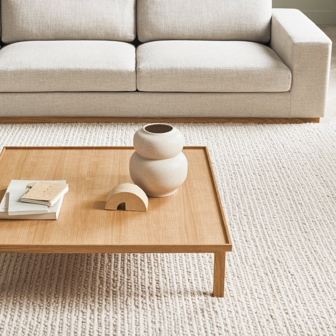 Neutral beige sofa, natural wood coffee table, textured cream rug; minimalistic design with soft tones and subtle patterns.