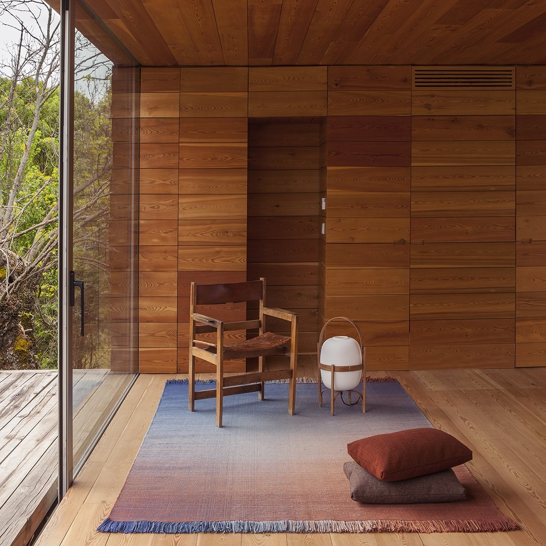 Soft gradient rug in blue, lavender, and orange tones, complemented by warm wooden textures and earthy cushions.