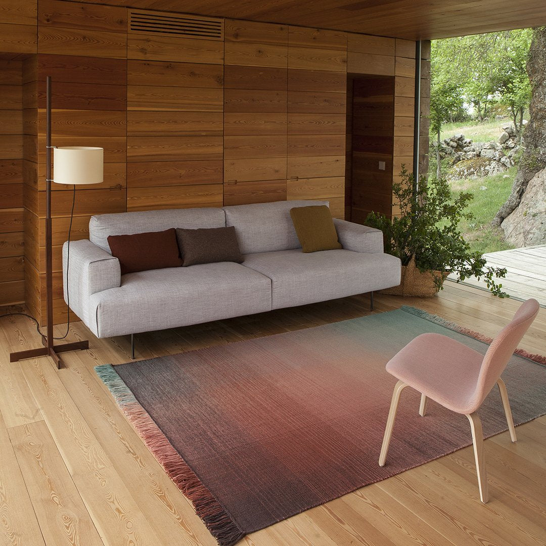 Soft gray sofa with earth-toned cushions, paired with a gradient rug transitioning from deep red to soft pink.