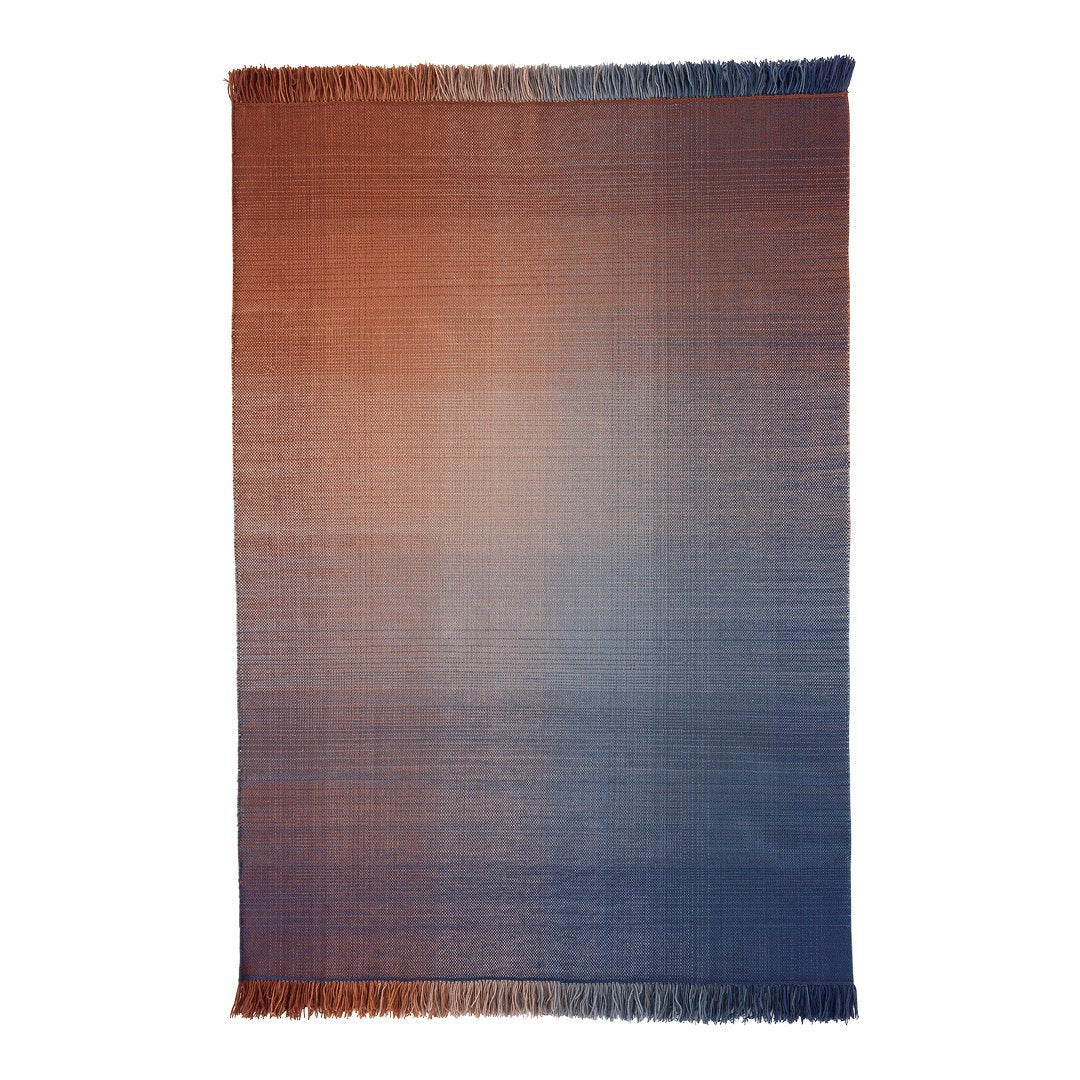 "Gradient woven blanket with warm orange to cool blue ombre, featuring soft fringed edges."