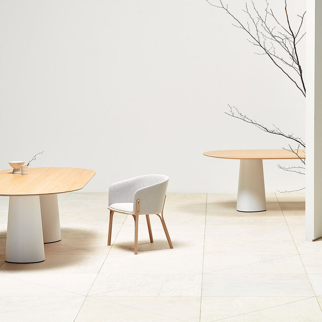 Light wood tables and a gray upholstered chair set against a neutral backdrop, featuring clean lines and minimal patterns.