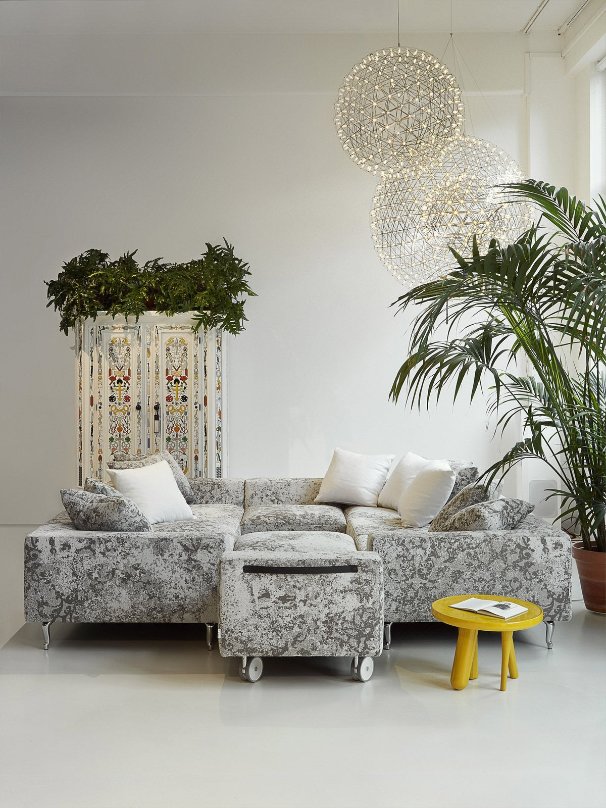 Gray and white patterned sectional sofa with accent pillows, complemented by vibrant yellow side table and lush greenery.