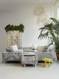 Gray and white patterned sectional sofa with accent pillows, complemented by vibrant yellow side table and lush greenery.