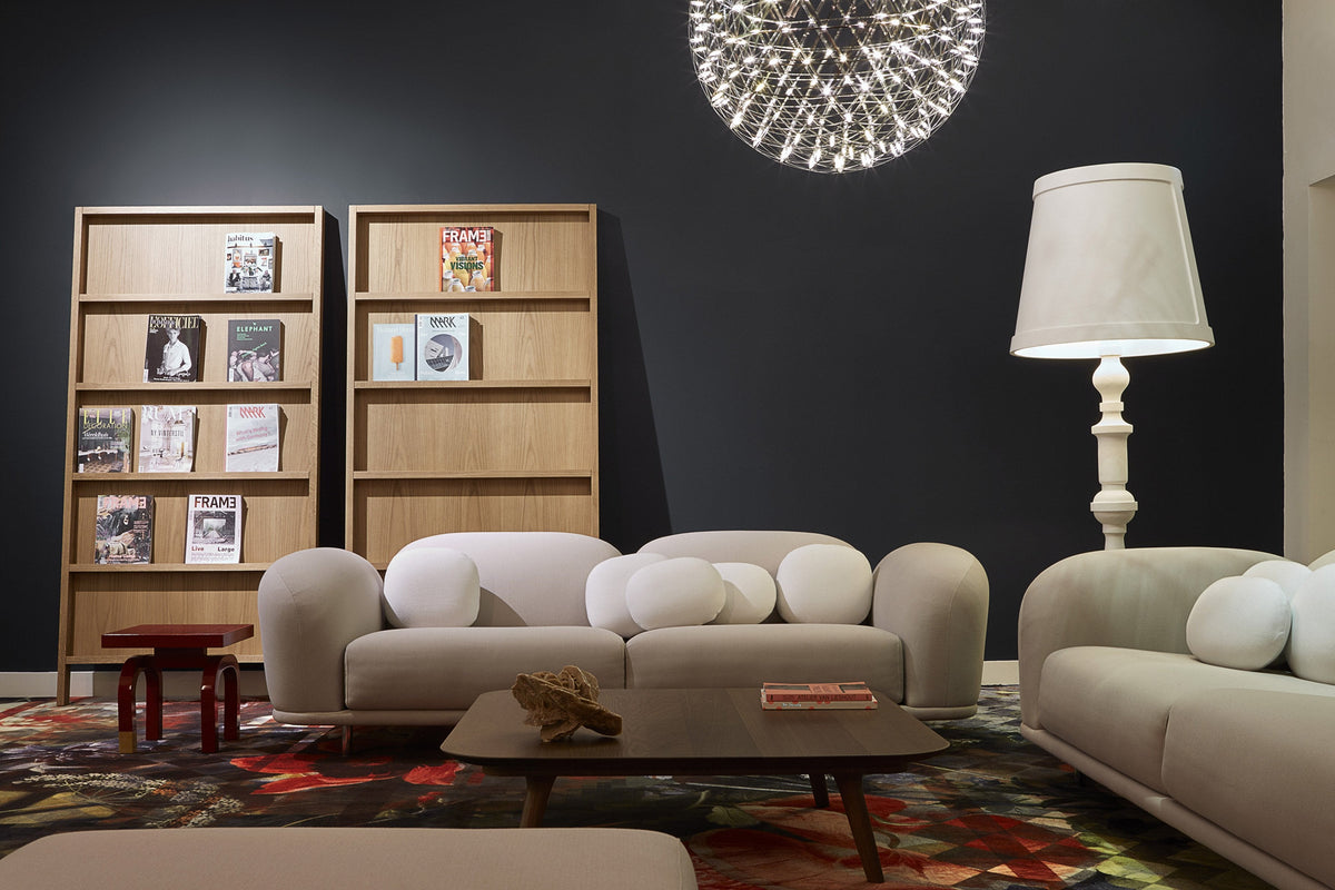 Modern lounge with neutral beige sofas, bright white cushions, and a patterned multicolor area rug against a dark wall.