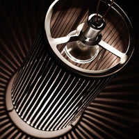 Industrial-style pendant lamp with metallic tones and sleek vertical lines creating shadow patterns.