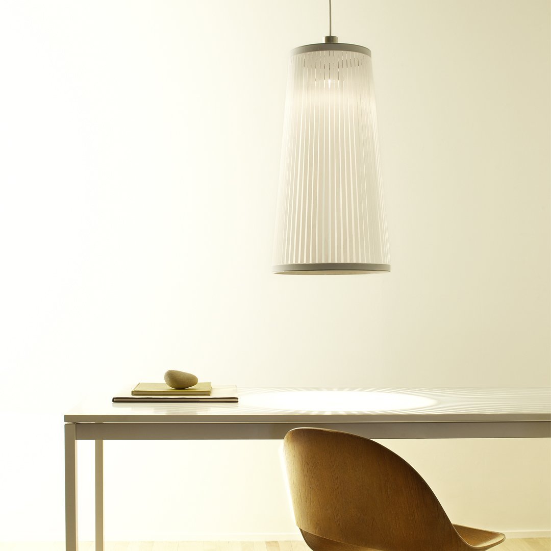 White pleated pendant light with a sleek metallic top, illuminating a minimalist wooden table and chair.