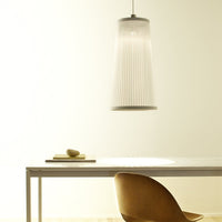 White pleated pendant light with a sleek metallic top, illuminating a minimalist wooden table and chair.