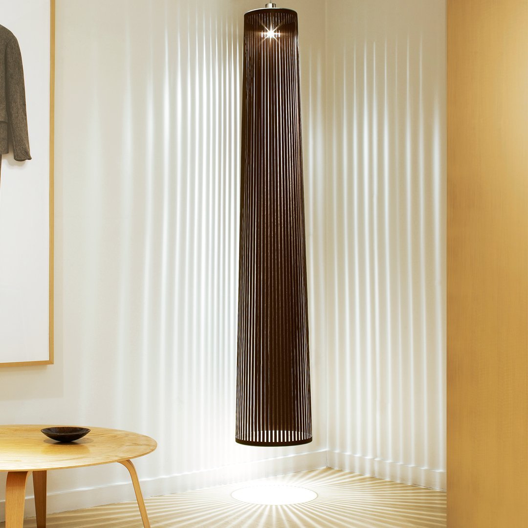 Tall, cylindrical pendant light in dark brown with delicate vertical strands, casting soft light patterns on the floor.