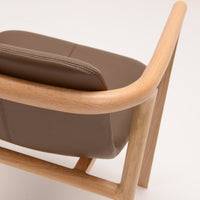 Brown leather chair with a smooth finish and natural wood armrests, featuring minimalist design and clean lines.