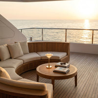 Sunset glow over a cozy, circular beige sofa with brown wooden accents and a round coffee table on a deck.