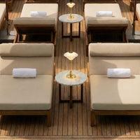 Beige lounge chairs with white towels, surrounded by light-colored marble tables on a wooden deck. Elegant summer vibe.