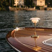 Elegant gold and white lamp atop a polished wooden boat, featuring intricate striped patterns reflecting on water.