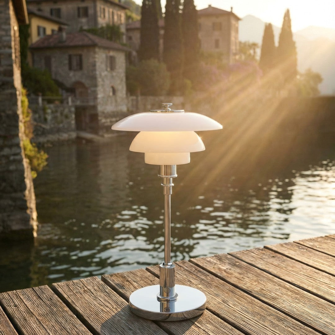 Modern white and chrome lamp with layered shade design, reflecting soft light by a lakeside setting.