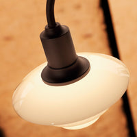 Sleek, glossy white glass pendant light with a black metal fixture, set against a warm, natural wood background.