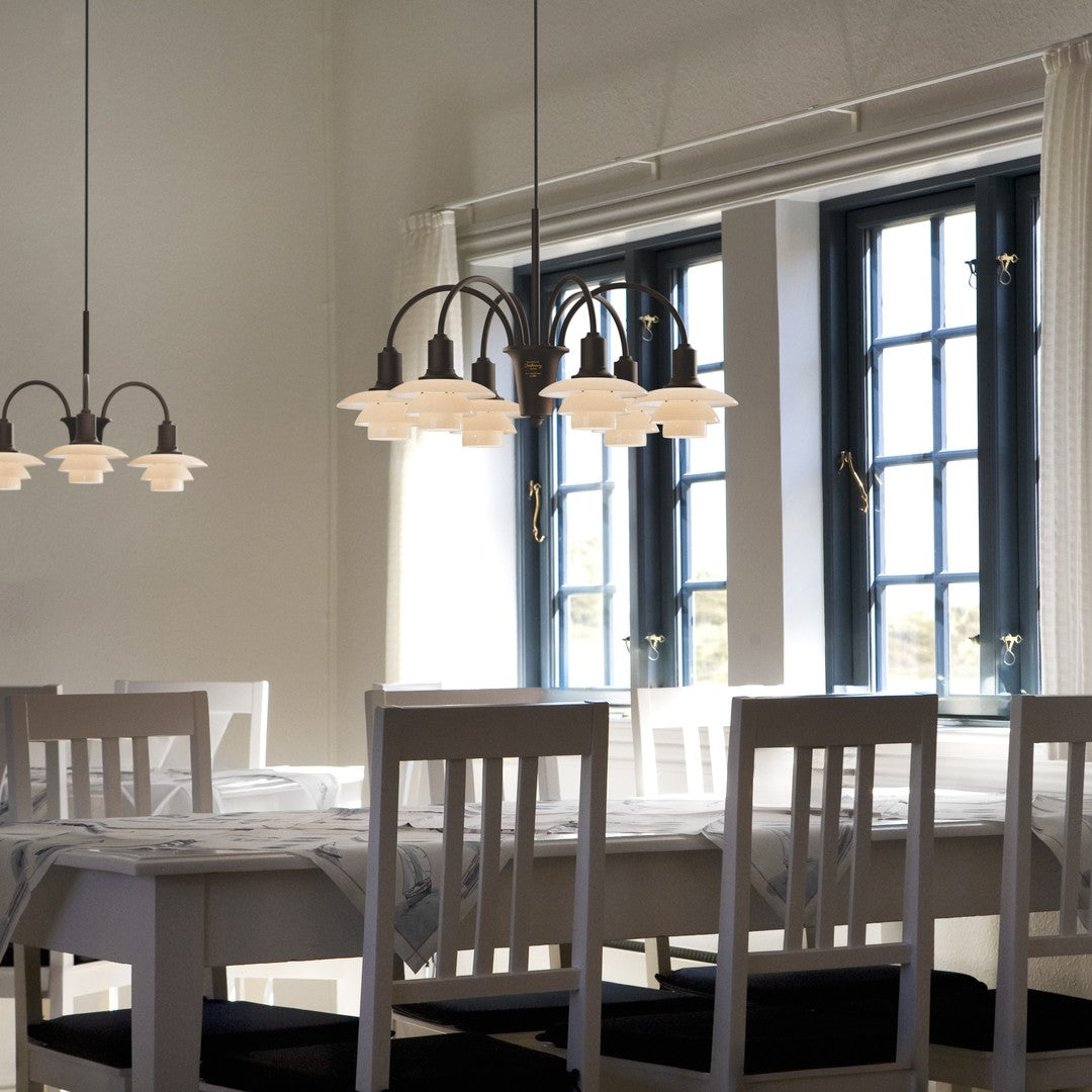 "White dining table and chairs with elegant glass pendant lights in a bright room featuring dark blue window frames."