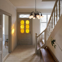 Modern hallway with gray walls, light wood flooring, and a yellow patterned door accented by a stylish chandelier.