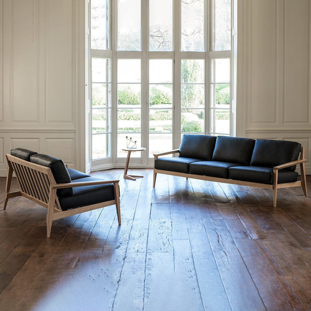 Black leather sofa with light wood accents, featuring clean lines and a modern design in a spacious, bright room.