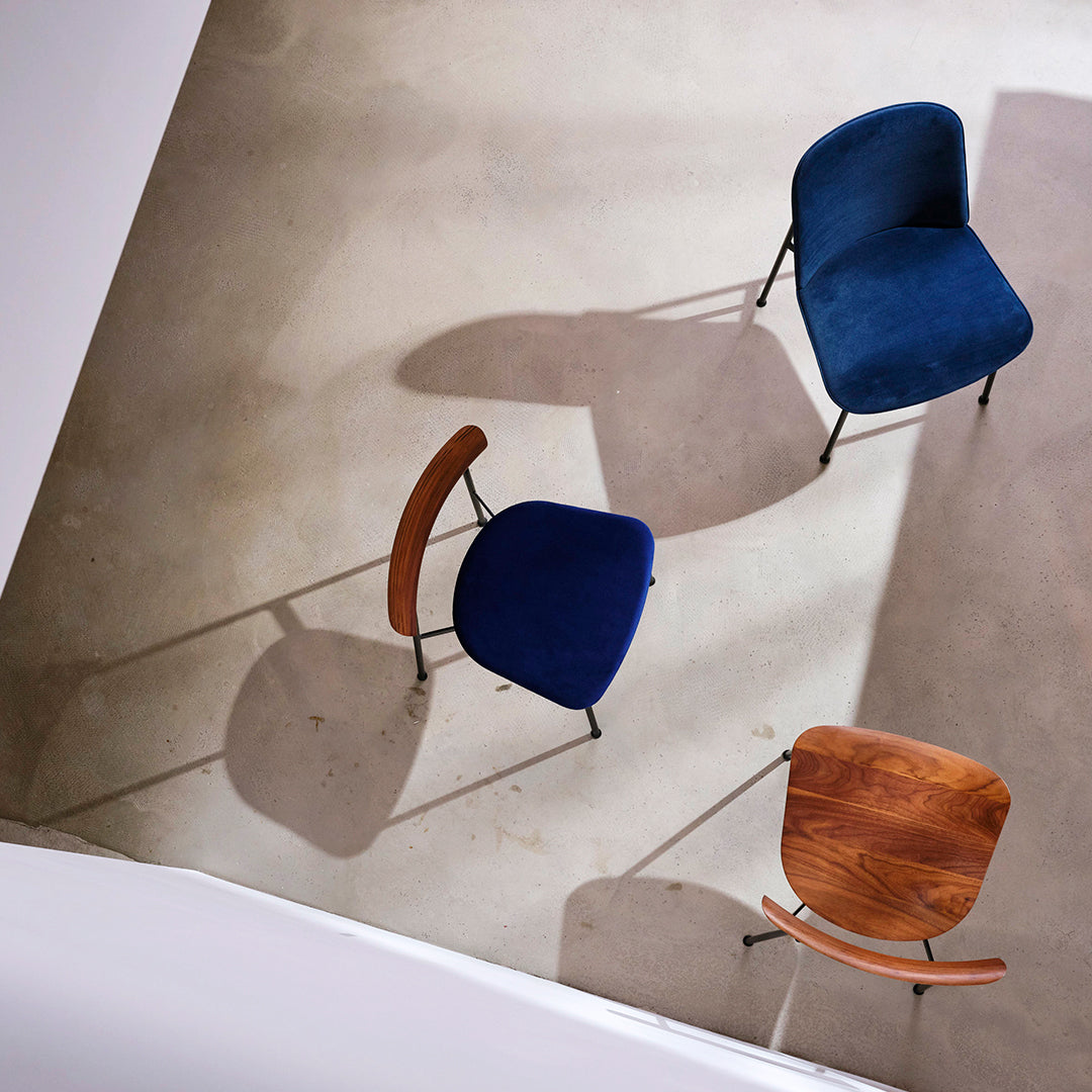 Three stylish chairs featuring deep blue upholstery and warm wood accents, casting unique shadows on a neutral floor.