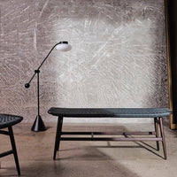 Gray patterned bench with dark wood legs, paired with a minimalist black lamp against a textured wall.