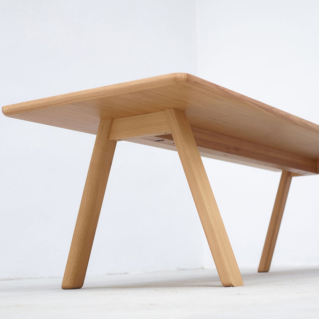 Light wooden table with a smooth finish and minimalist design, featuring natural wood grain patterns and tapered legs.