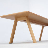 Light wooden table with a smooth finish and minimalist design, featuring natural wood grain patterns and tapered legs.