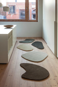 Abstract, organic-shaped rugs in earthy tones: beige, dark green, light gray, and rich brown, complementing modern interiors.