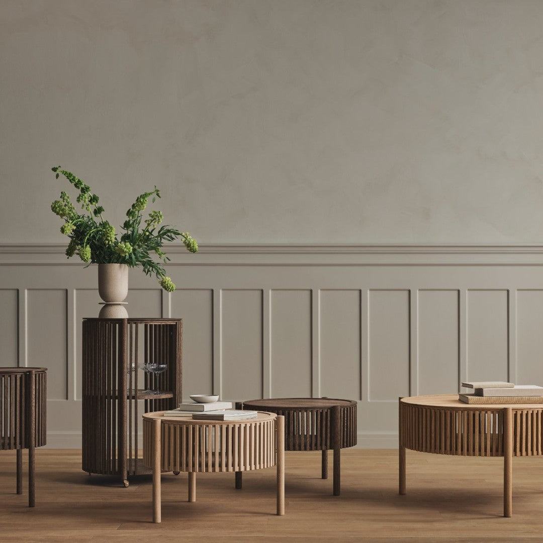 "Natural wood coffee tables in light and dark finishes with vertical slats, styled with greenery in a modern setting."