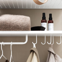 Soft beige sweater, black hair comb, and brown spray bottles on a white shelf against a neutral wall. Modern and minimalist.