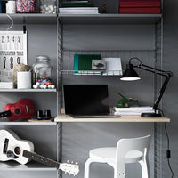 Modern desk setup featuring gray shelving, green accents, and colorful decor with a minimalist white chair.