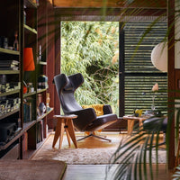 Black leather chair with wooden legs, surrounded by green foliage and warm wood accents in a modern living space.