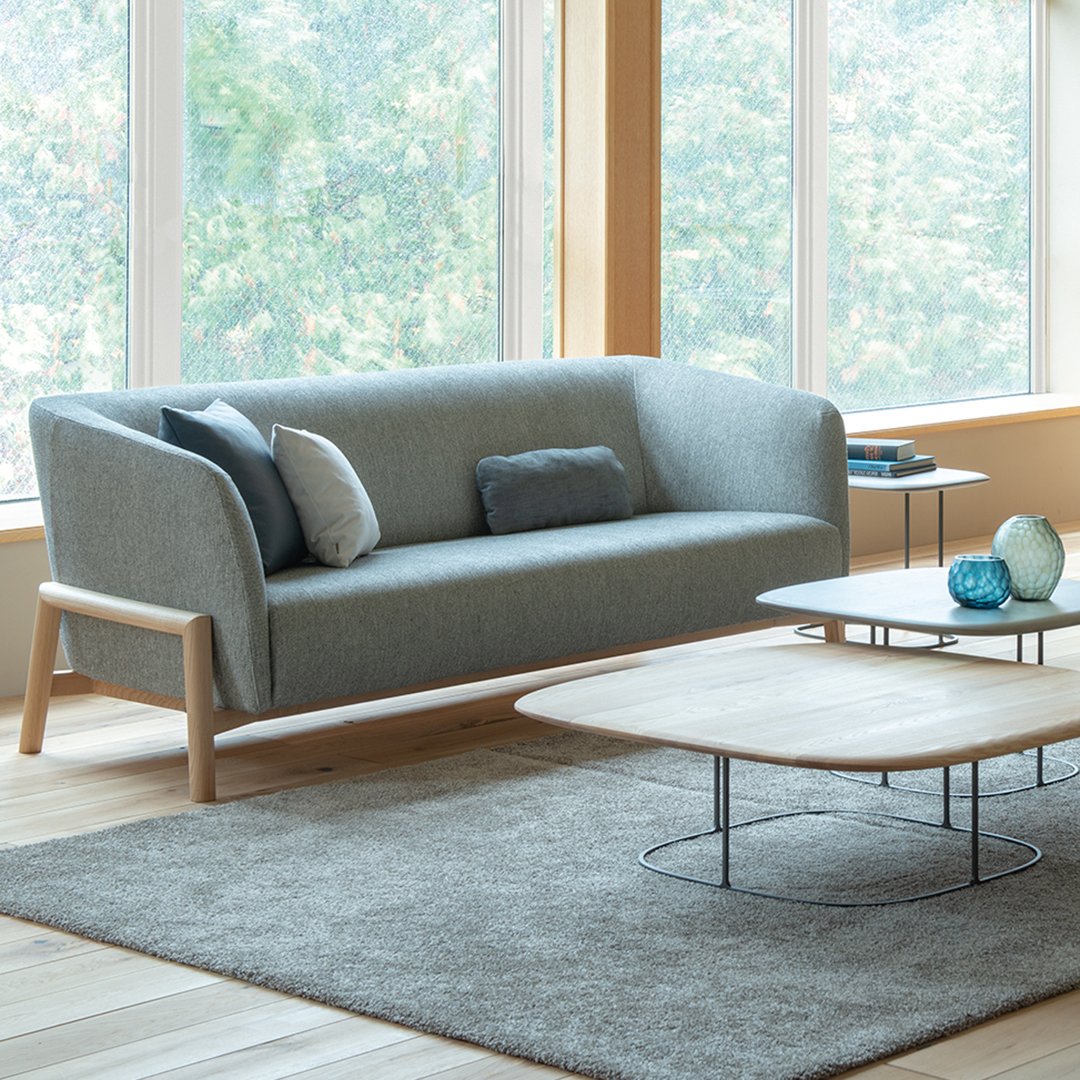 Gray fabric sofa with light wooden legs, accompanied by a gray rug and minimalist coffee table, in a bright, airy setting.