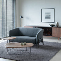 Sleek grey sofa with minimalist wooden accent tables, set on a textured gray rug in a modern room.