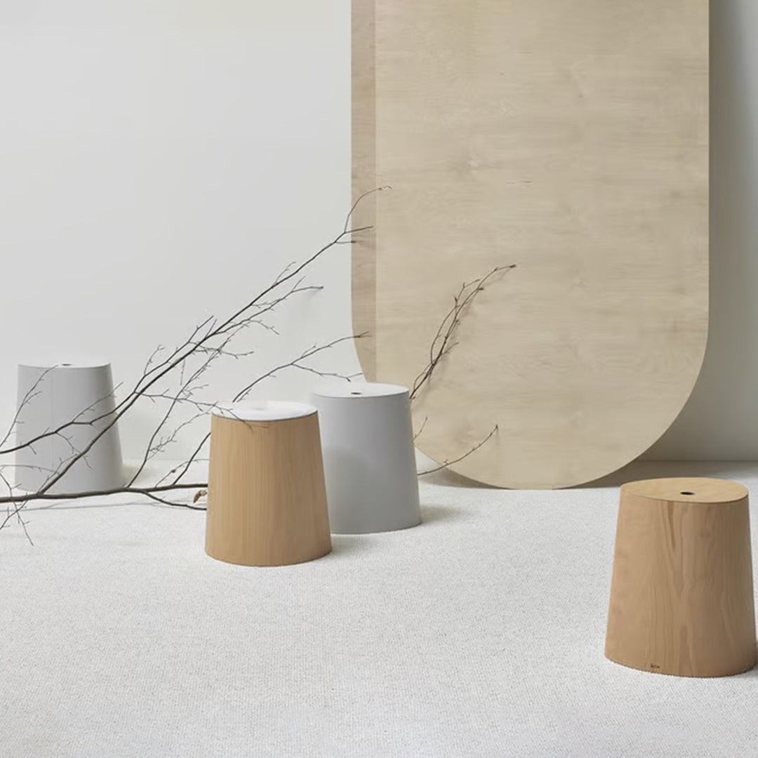 Three modern stools in natural wood, white, and gray against a minimalist backdrop with smooth curved shapes.