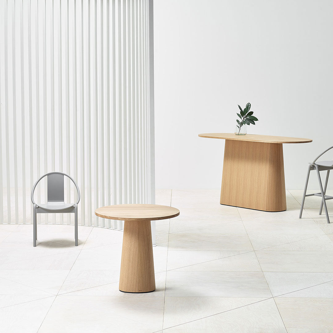 Minimalist wooden tables in light oak finish, featuring smooth curves and soft beige flooring with white vertical blinds.